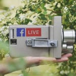 a hand holding an old video camera with a facebook sticker